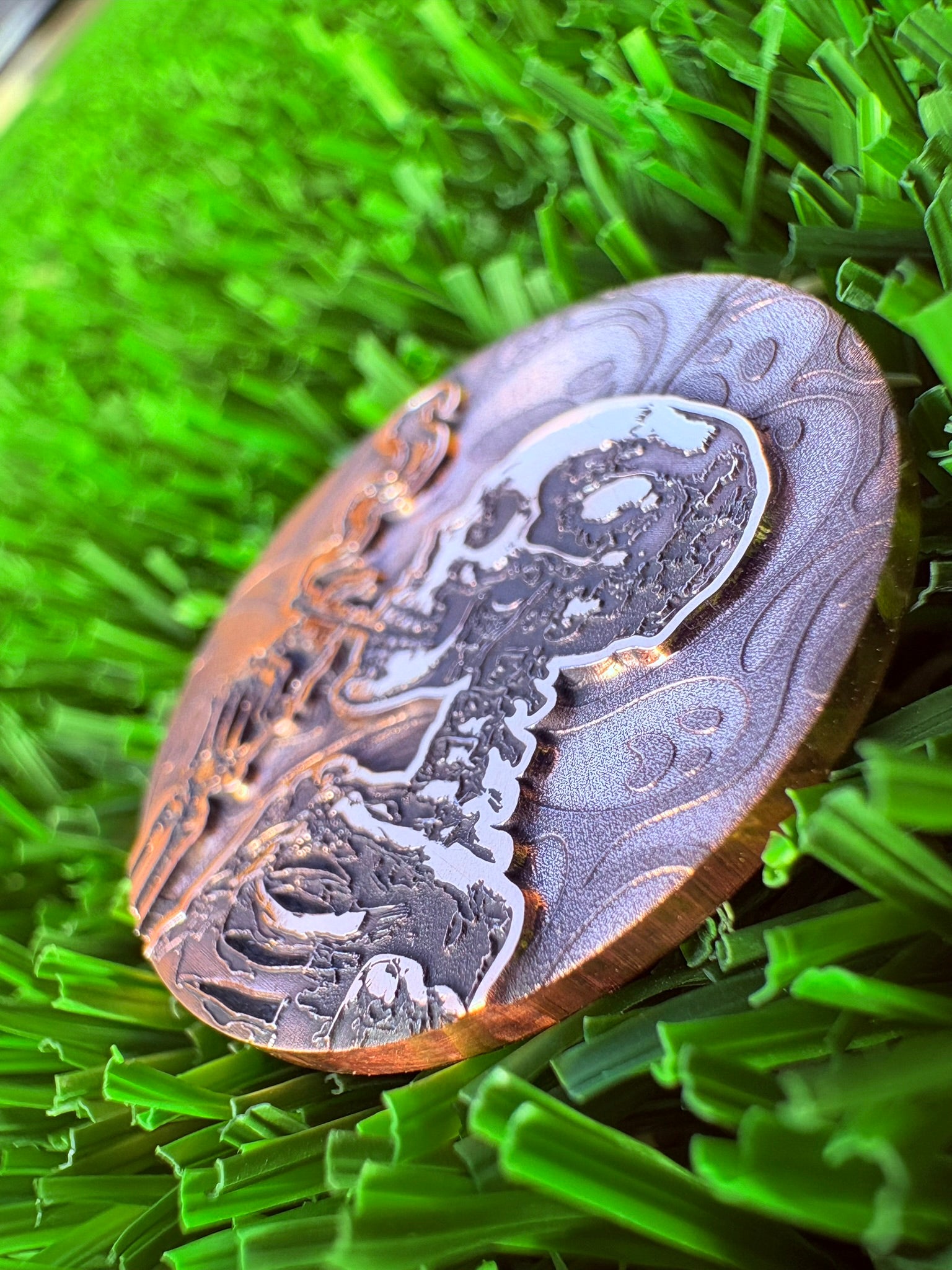 Decorative golf ball marker with intricate patterns on a green grass background