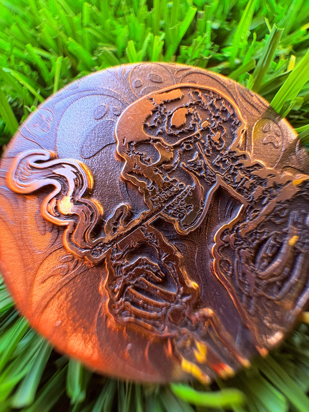Bronze golf ball marker with intricate design on grass