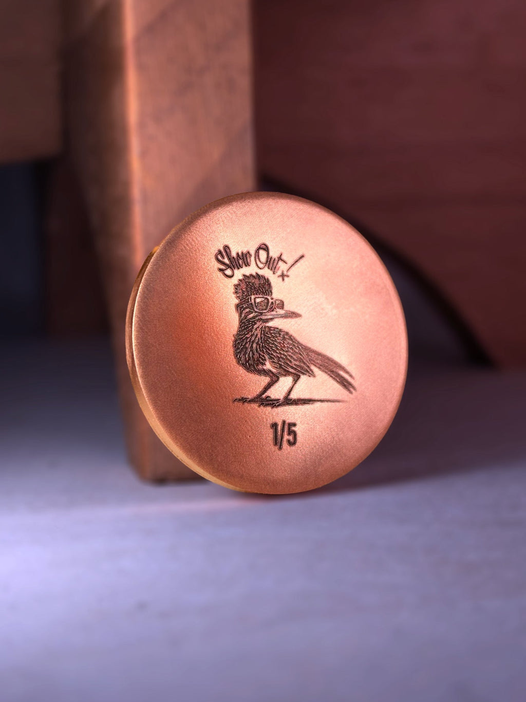 Copper ball marker with engraved design on a wooden surface
